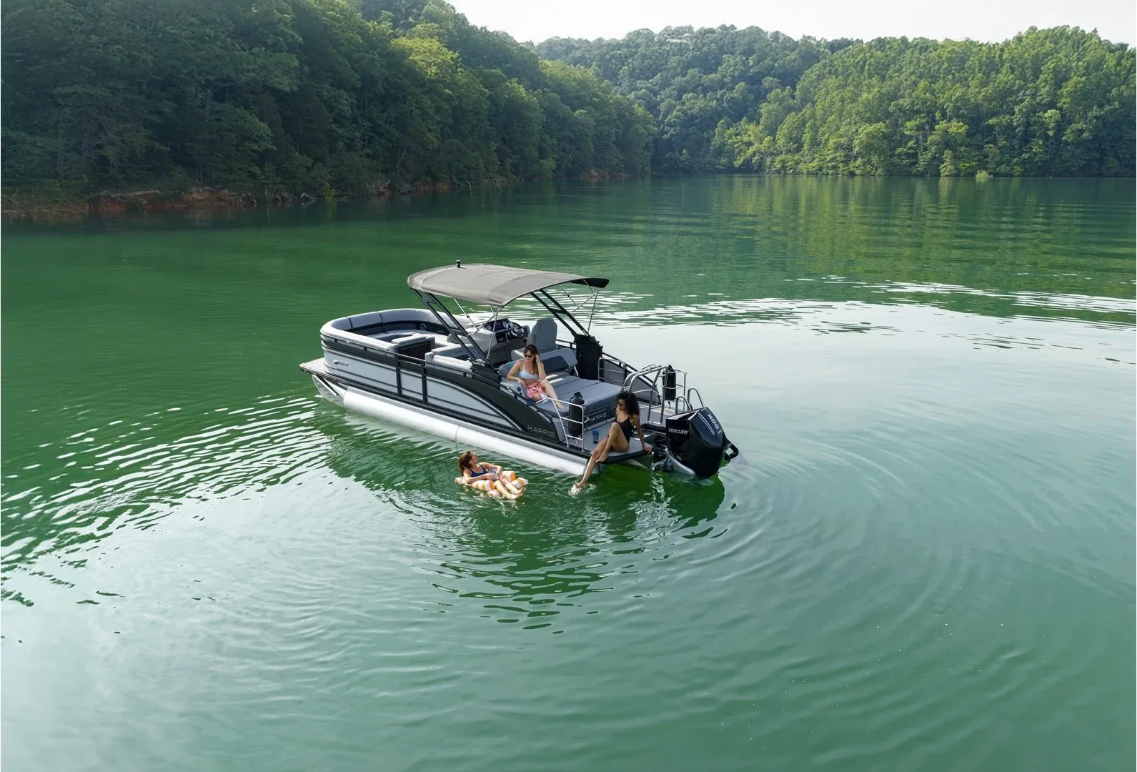 Harris Solstice 250 SL anchored on a wooded lake while passengers swim